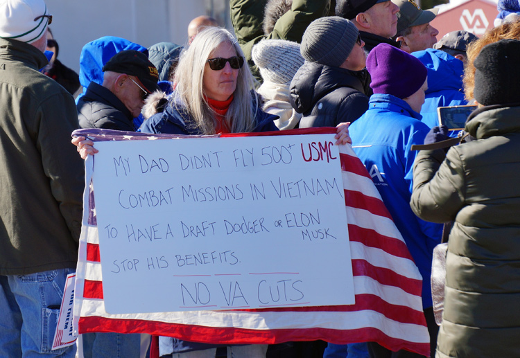 Woman holds sign that says her dad did not fly 500 combat missions to have a draft dodger or Elon Musk stop his benefits