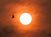 Helicopter flying through orange sky at sunset caused by Canadian wildfires