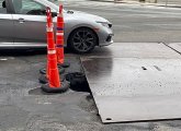 Large roadway hole covered by metal plate and traffic cones