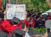 Student holds sign in protest against David Zaslow, far right