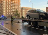 Firefighters clean up debris as car awaits transport away from the scene