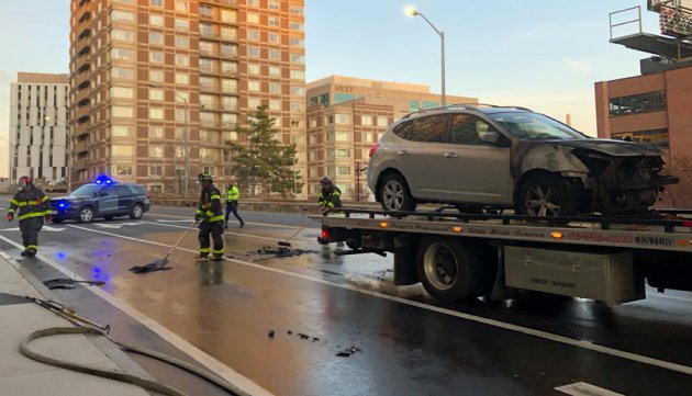 Firefighters clean up debris as car awaits transport away from the scene