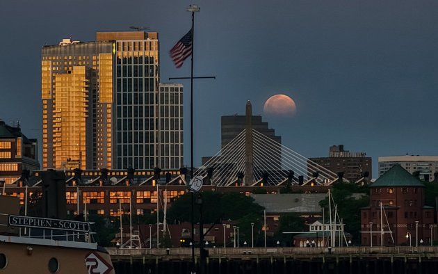 Sunlight reflects off one side of building while the moon goes down on the other