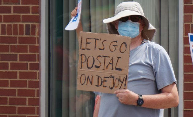 Man with sign that reads: Let's go Postal on DeJoy