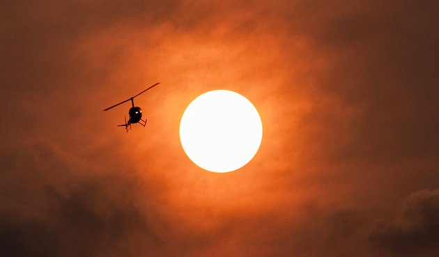 Helicopter flying through orange sky at sunset caused by Canadian wildfires