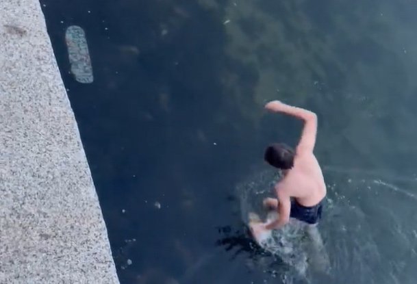 Man in Boston Harbor retrieving skateboard