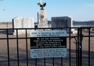 Fence around Worlld War II memorial at Castle Island with sign asking people to not try to clean stains