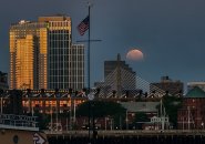 Sunlight reflects off one side of building while the moon goes down on the other