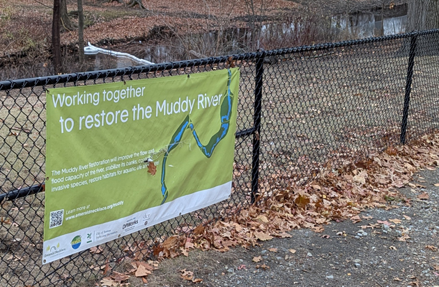 Sign advertising Muddy River cleanup project near a boom placed because of the oil